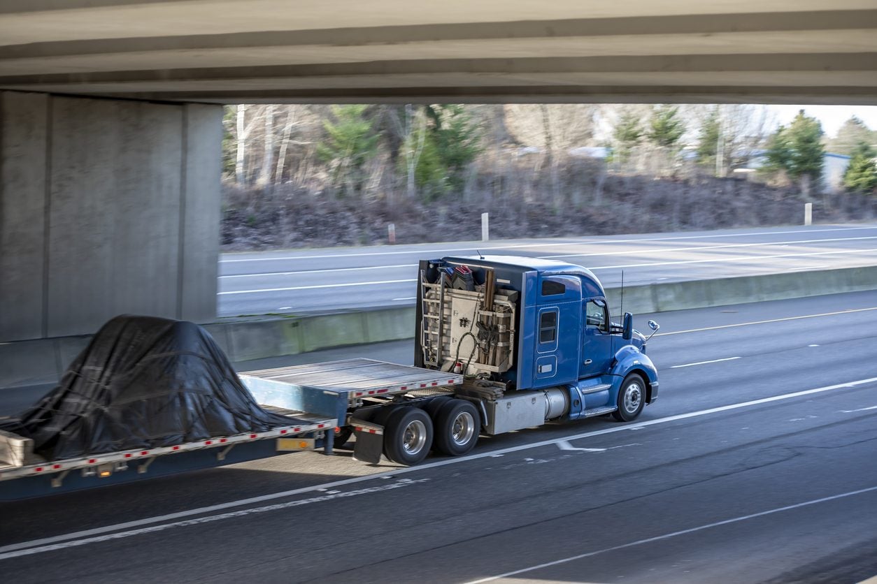 Blue tractor hauling a covered load under a bridge