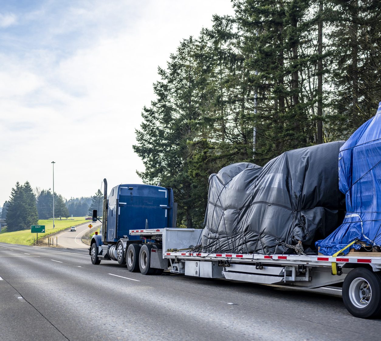 Blue conventional tractor hauling a covered load on a step deck