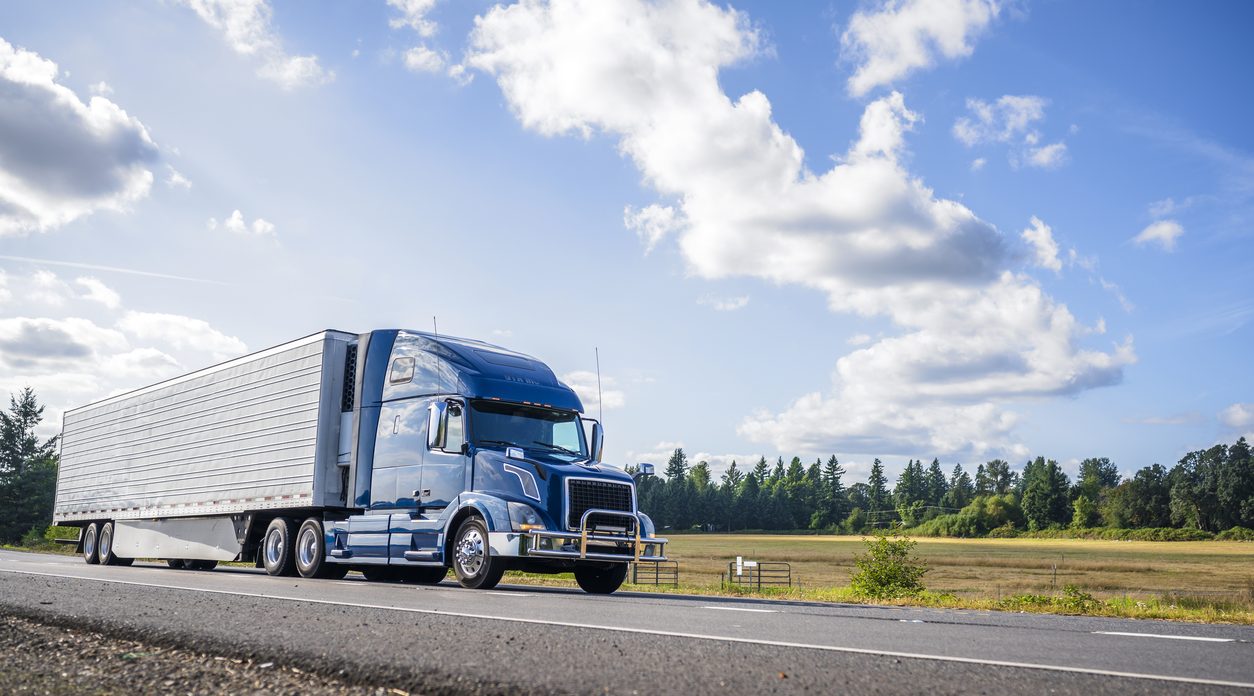 Blue conventional tractor with a refrigerated trailer on a straight road