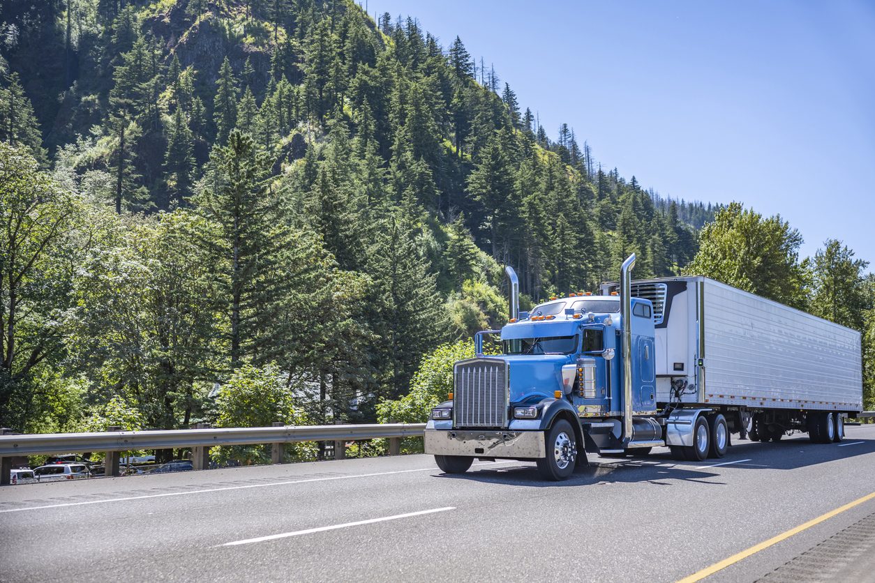 Blue conventional tractor with a reefer trailer on a mountain highway