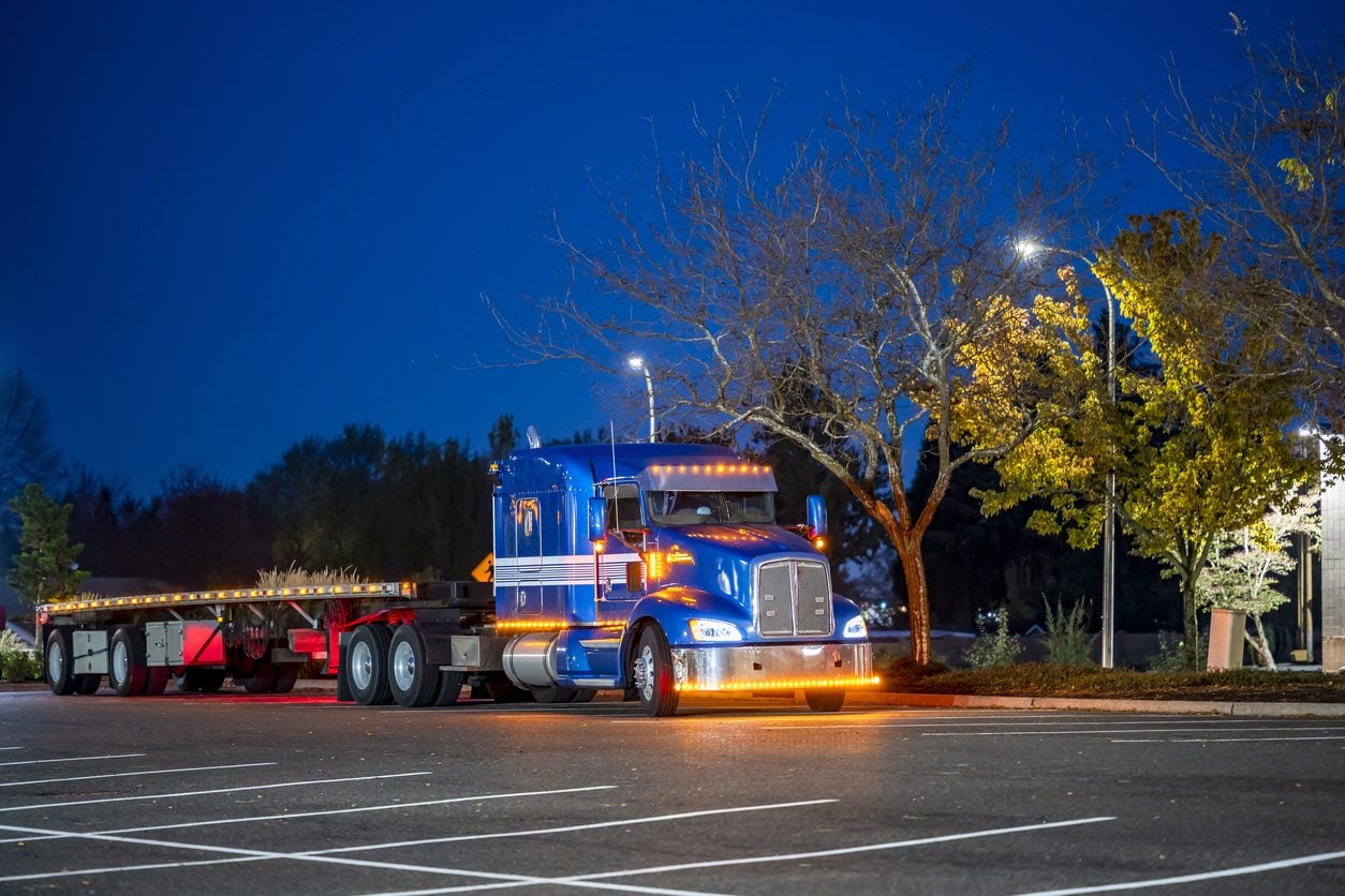 Classic tractor with a flatbed trailer at a truck stop at night