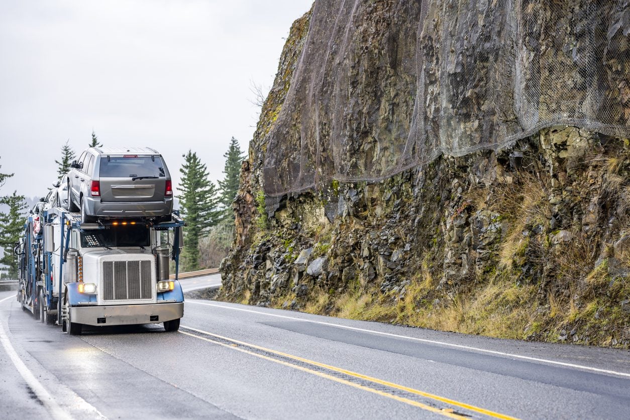 Car hauler loaded with vehicles on a wet mountain road