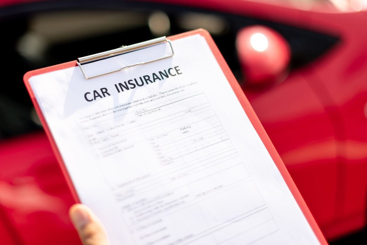Car insurance form on a clipboard held in front of a red car