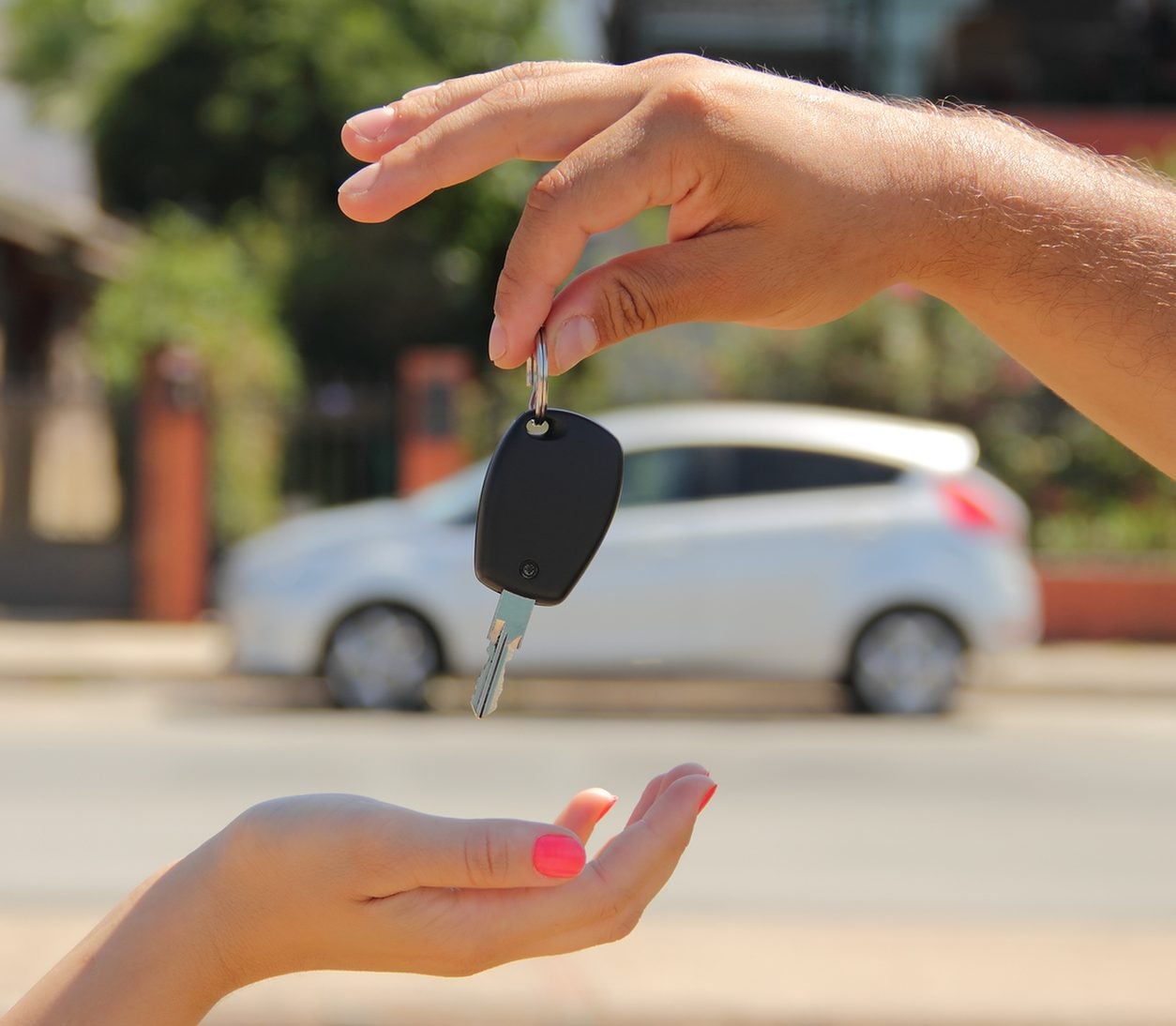 Car key being handed over beside a white car