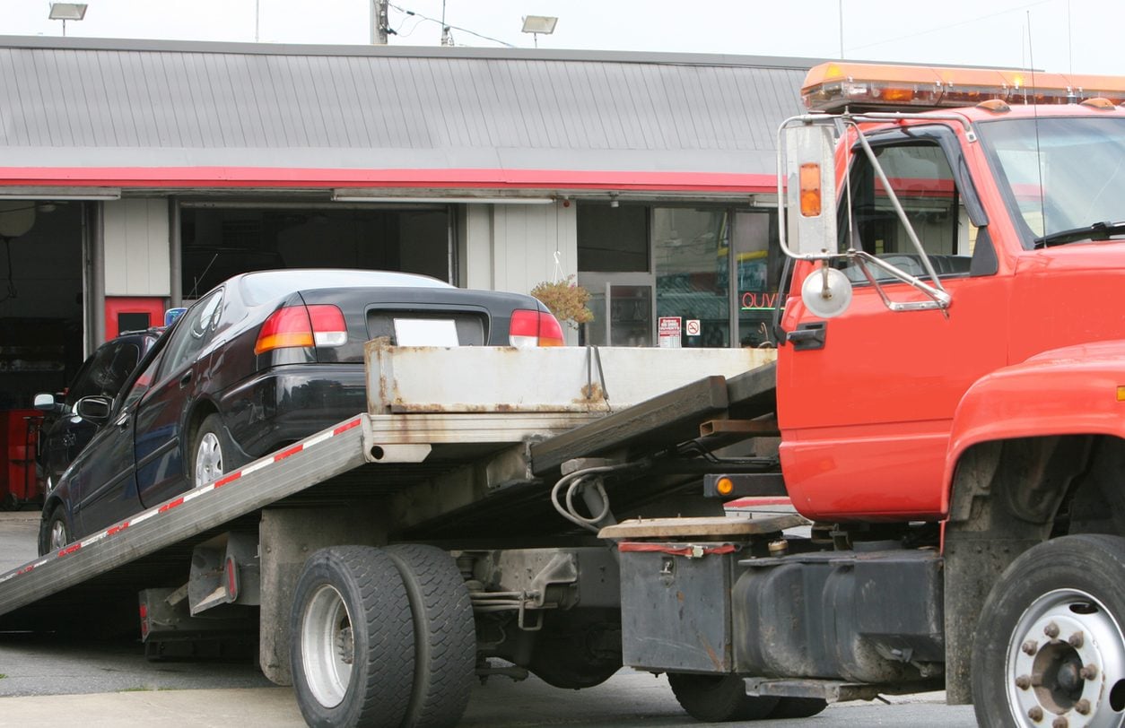 Car loaded onto the bed of a red rollback truck