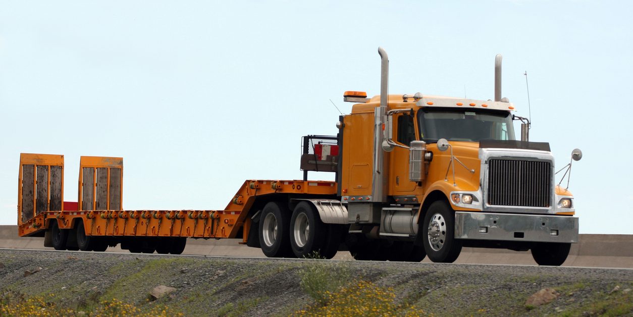 Orange conventional tractor with a low deck trailer