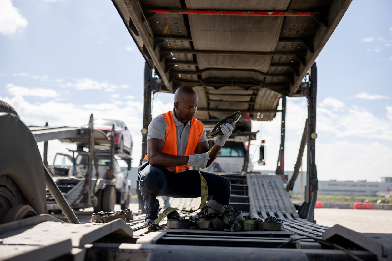 Driver fastening straps on the deck of a car hauling trailer