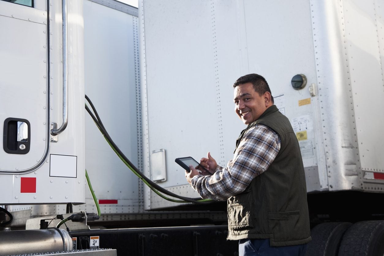 Truck driver checking a digital tablet beside a trailer
