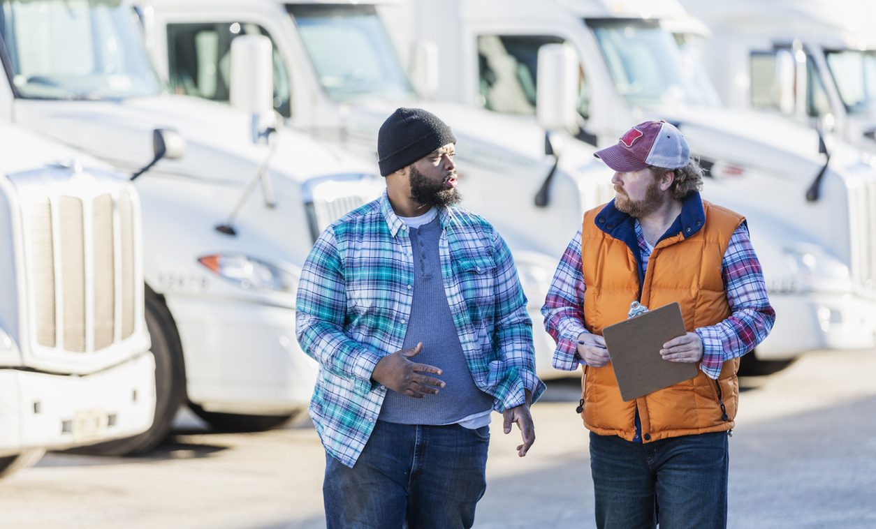 Two truck drivers talking with a clipboard beside a row of tractors