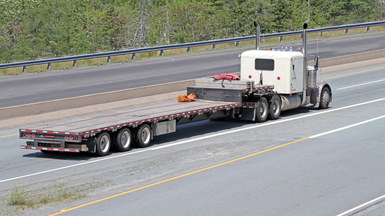 Conventional tractor with an empty flatbed trailer on a highway