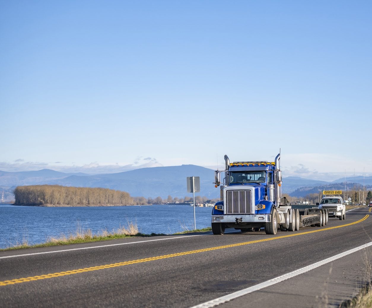 Escort car with a roof sign following an oversize load along a river highway