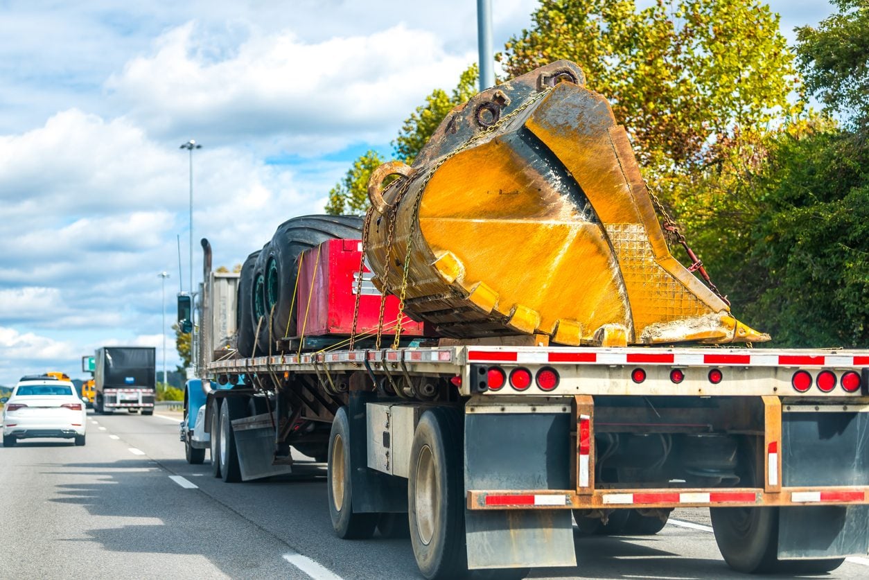 Excavator bucket and boom loaded on a flatbed in traffic