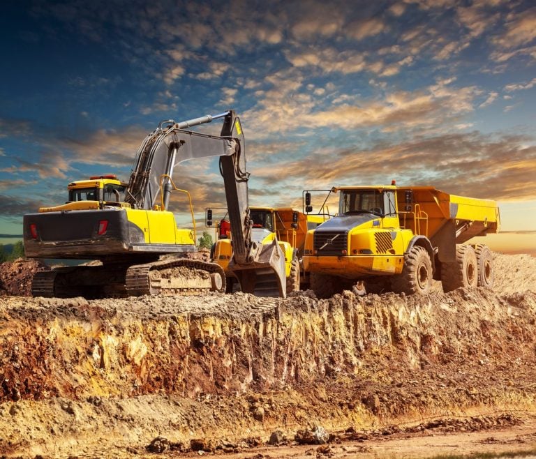 Excavator loading articulated dump trucks on a construction site