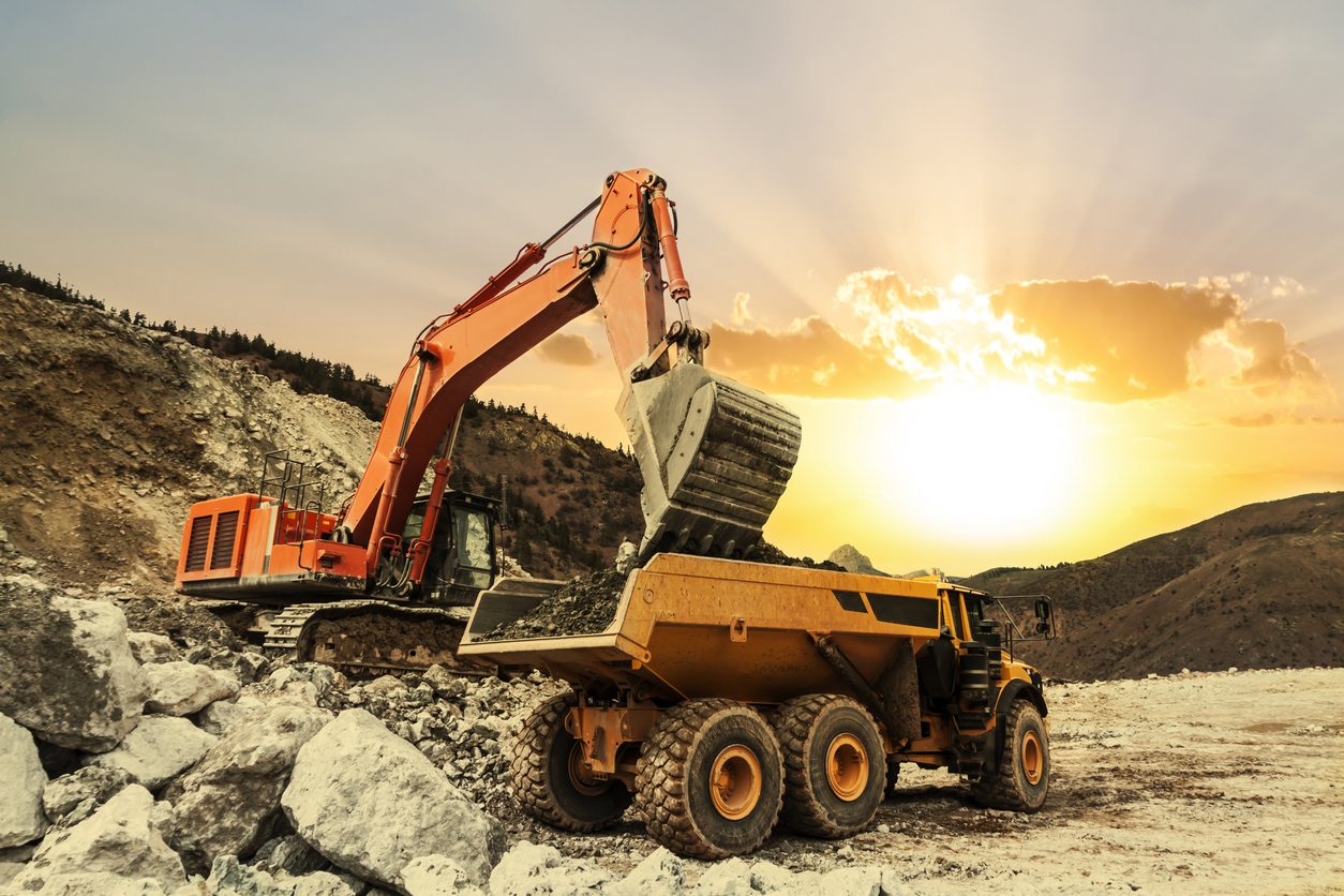 Excavator loading an articulated dump truck at sunset