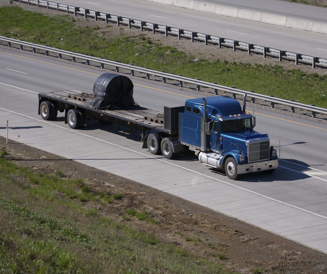 Flatbed truck carrying a single secured item on a highway