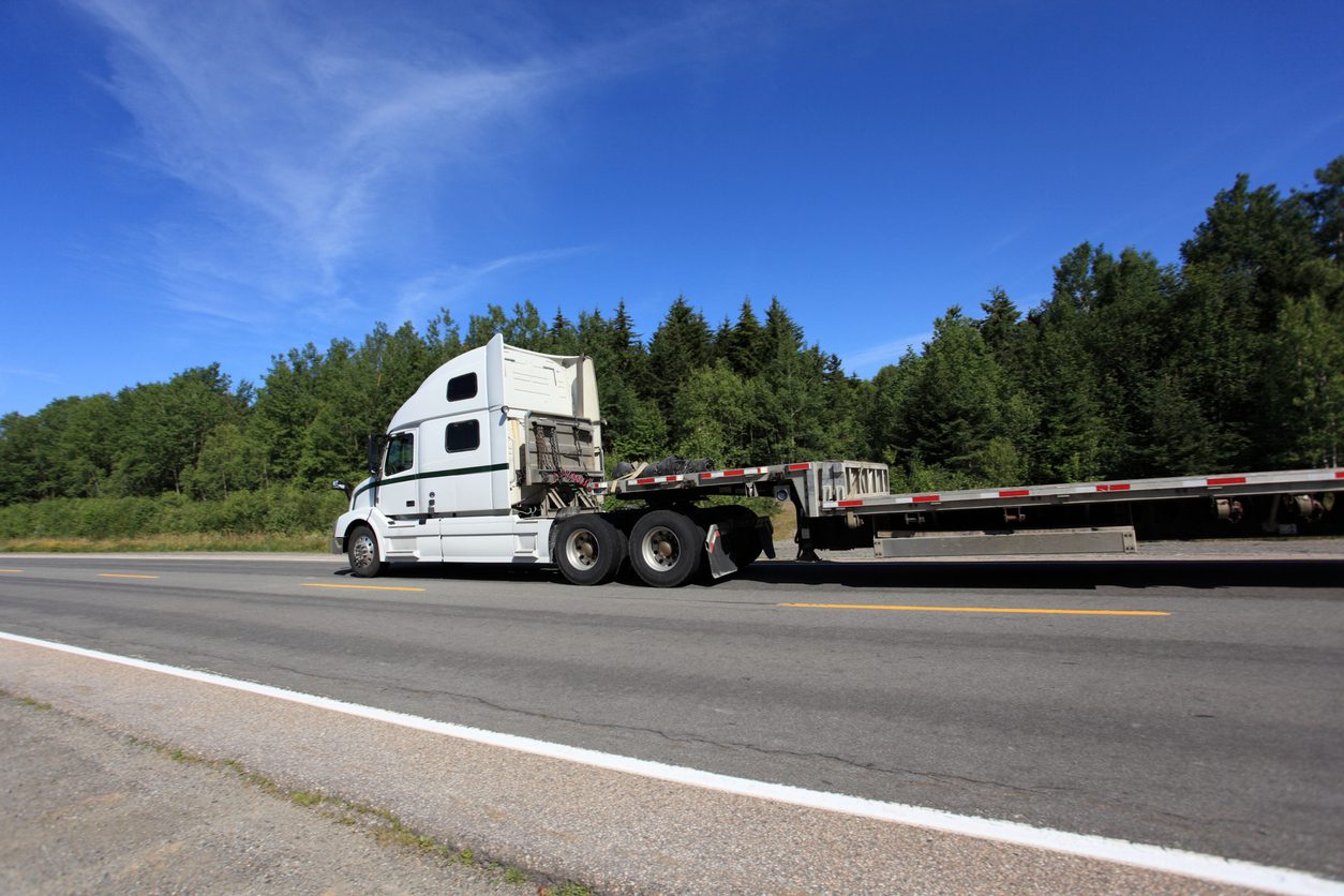 White conventional tractor with an empty flatbed trailer on a highway