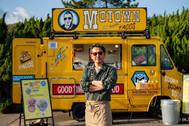 Food truck owner standing in front of his yellow taco truck