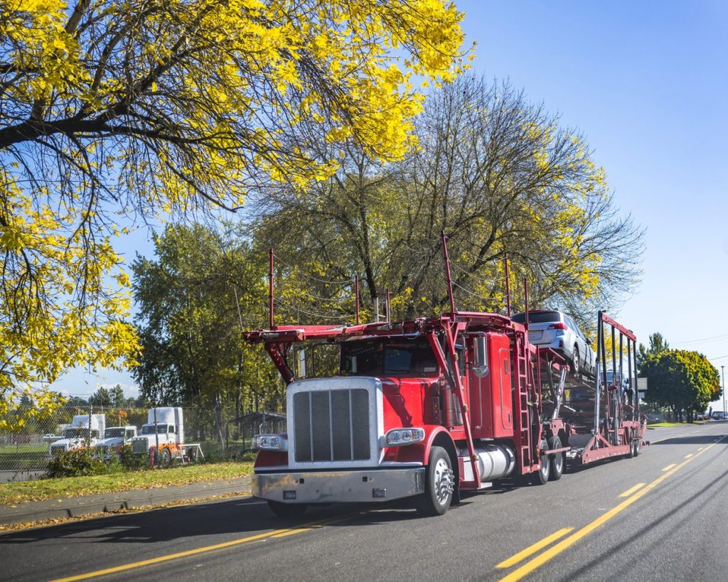 Red car hauler carrying a vehicle on a tree lined street
