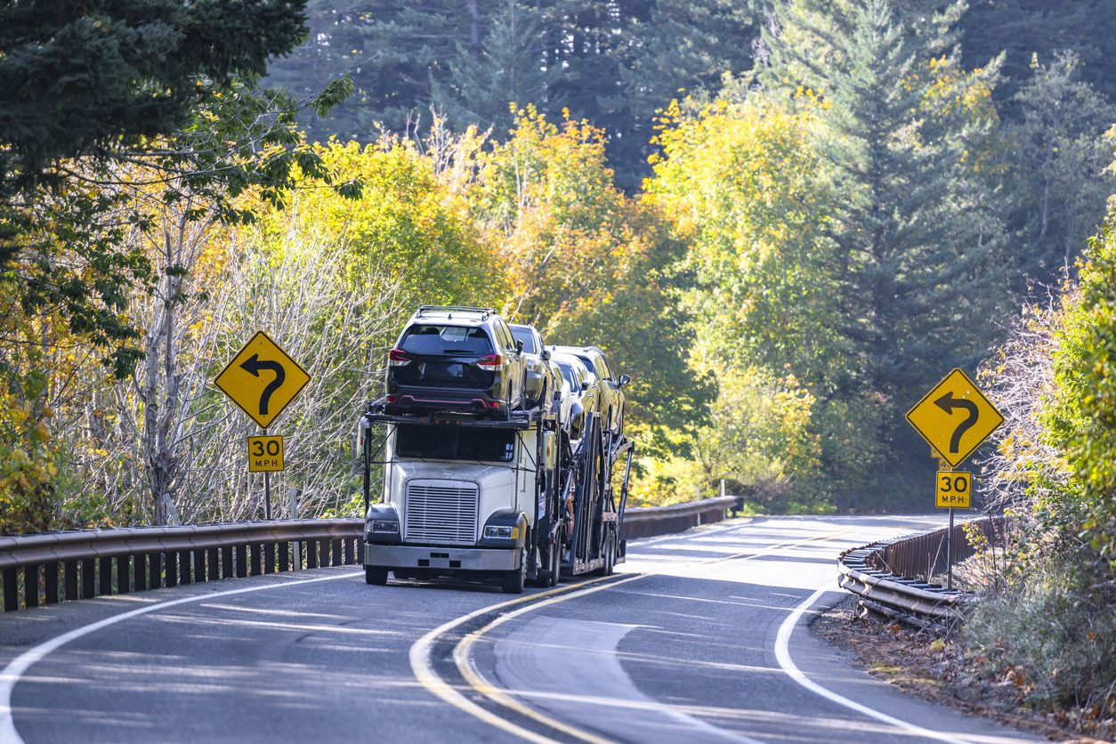 Loaded car hauler on a winding road through autumn forest