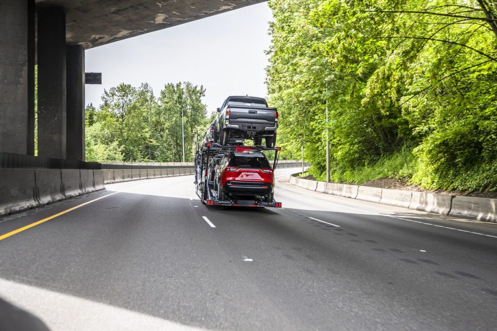 Car hauler loaded with pickup trucks passing under a bridge