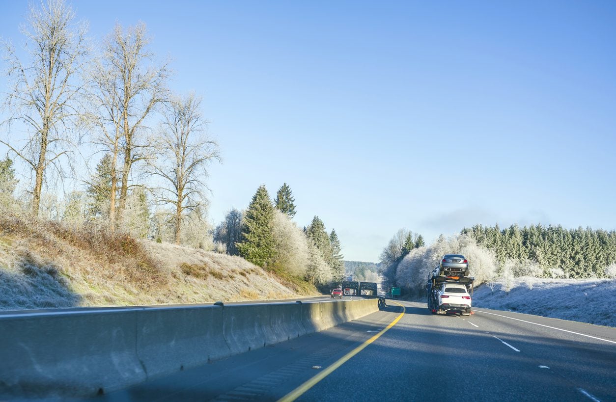 Car hauler on a straight highway with hills on both sides