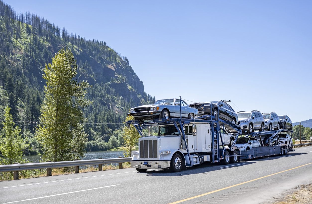 Loaded car hauler on a two lane road beside a river