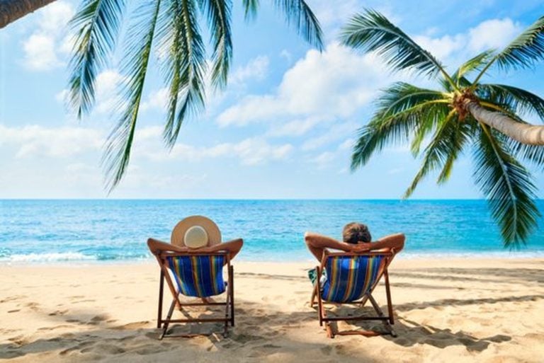 Couple relaxing in beach chairs under palms on a tropical shore
