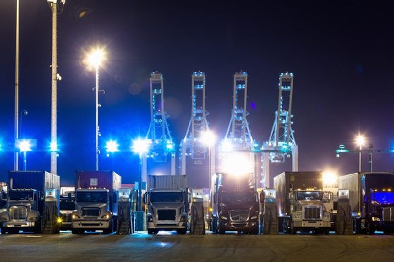 Trucks lined up beneath ship to shore cranes at the Port of Long Beach at night