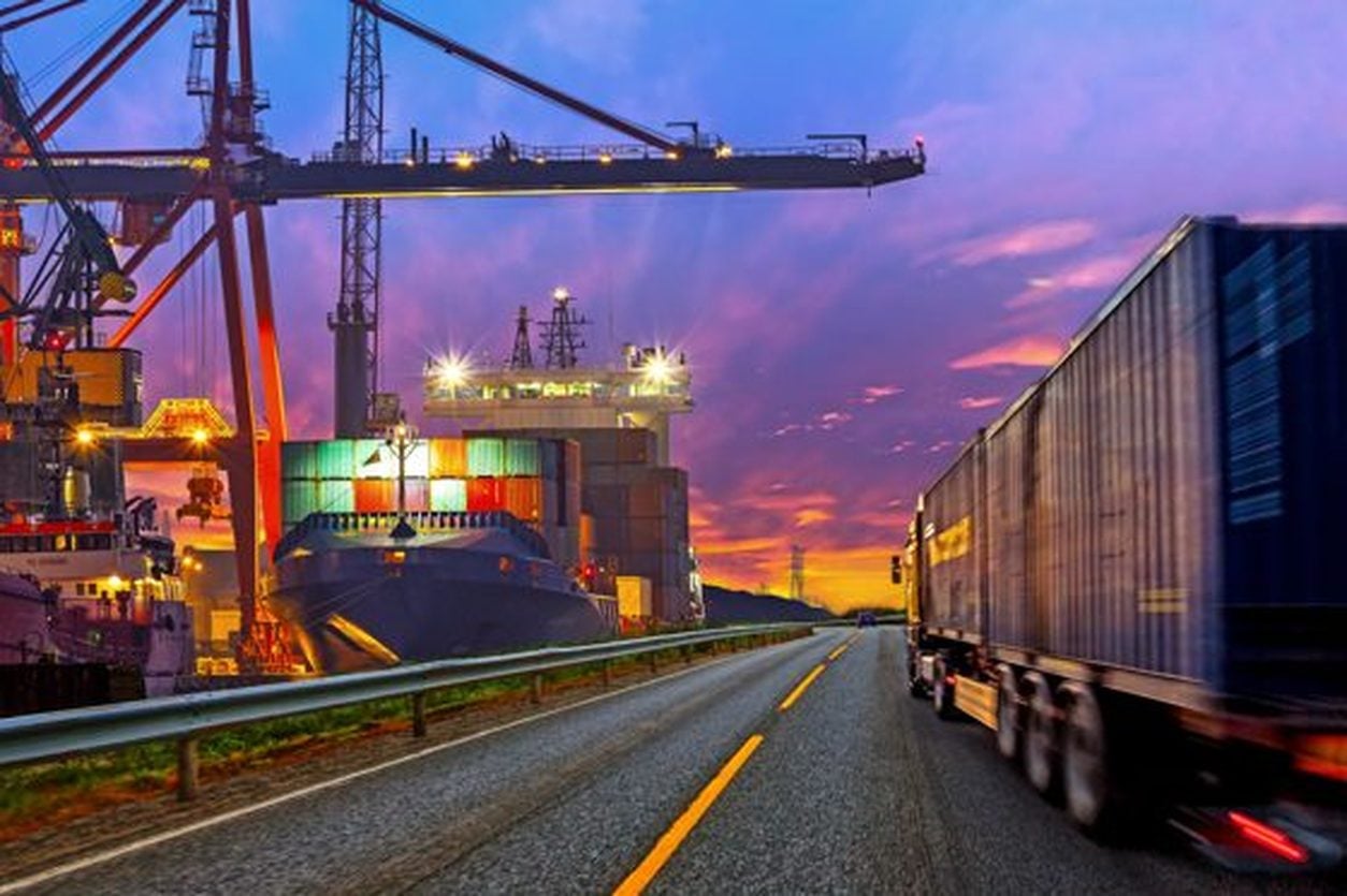 Container trucks at a port at sunset beside a cargo ship