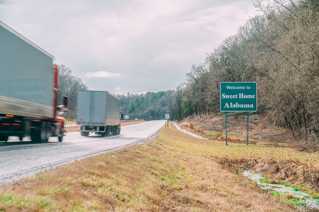 Two semi trucks passing a Welcome to Alabama sign on the interstate