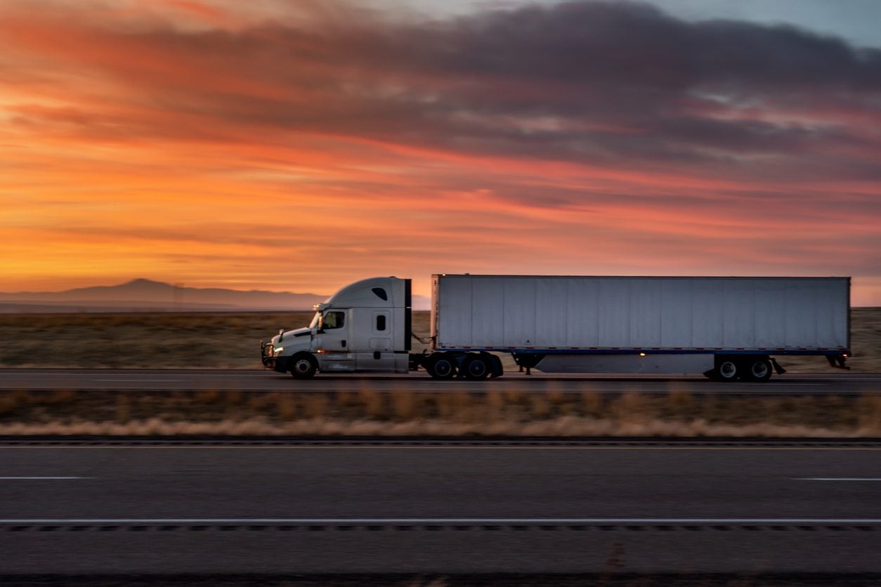 White conventional tractor and trailer on an interstate at sunset