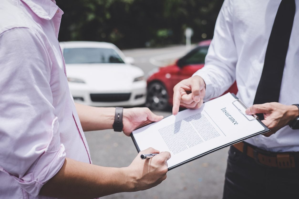 Completing a claim form beside a damaged vehicle