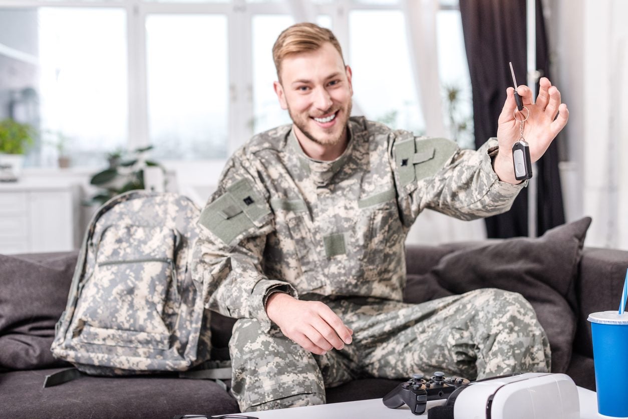 Service member at home holding a key beside packed gear