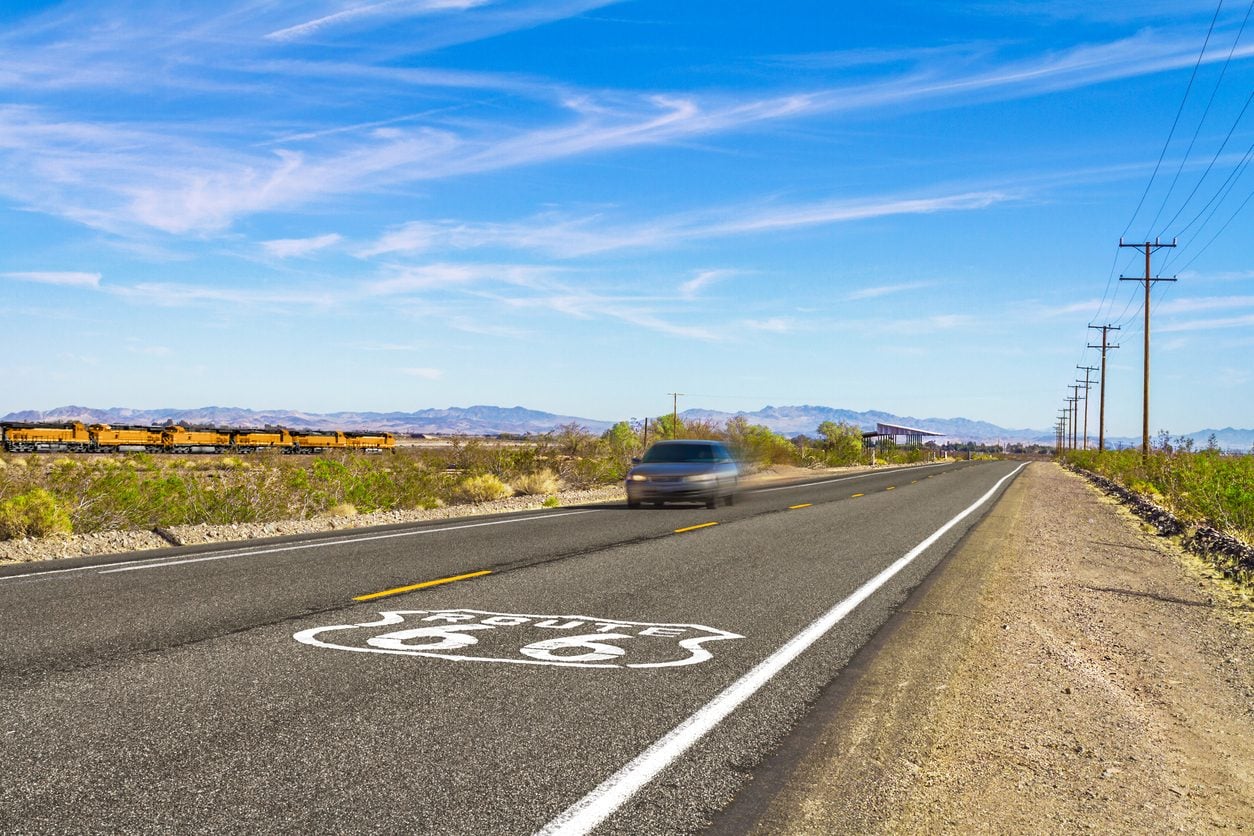 Freight train running beside a desert highway marked Route 66