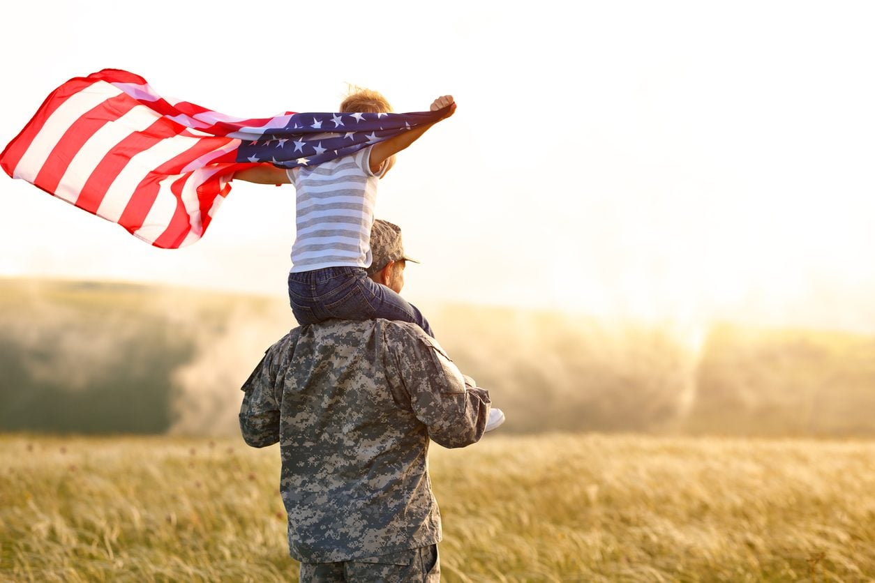 Child holding an American flag on a parent's shoulders at a homecoming