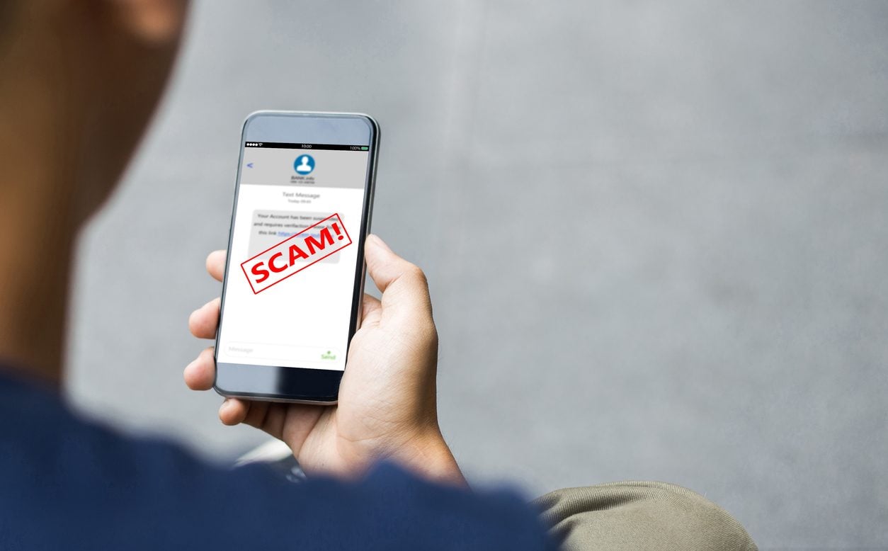 Person reading a fraudulent text message on a phone marked as a scam