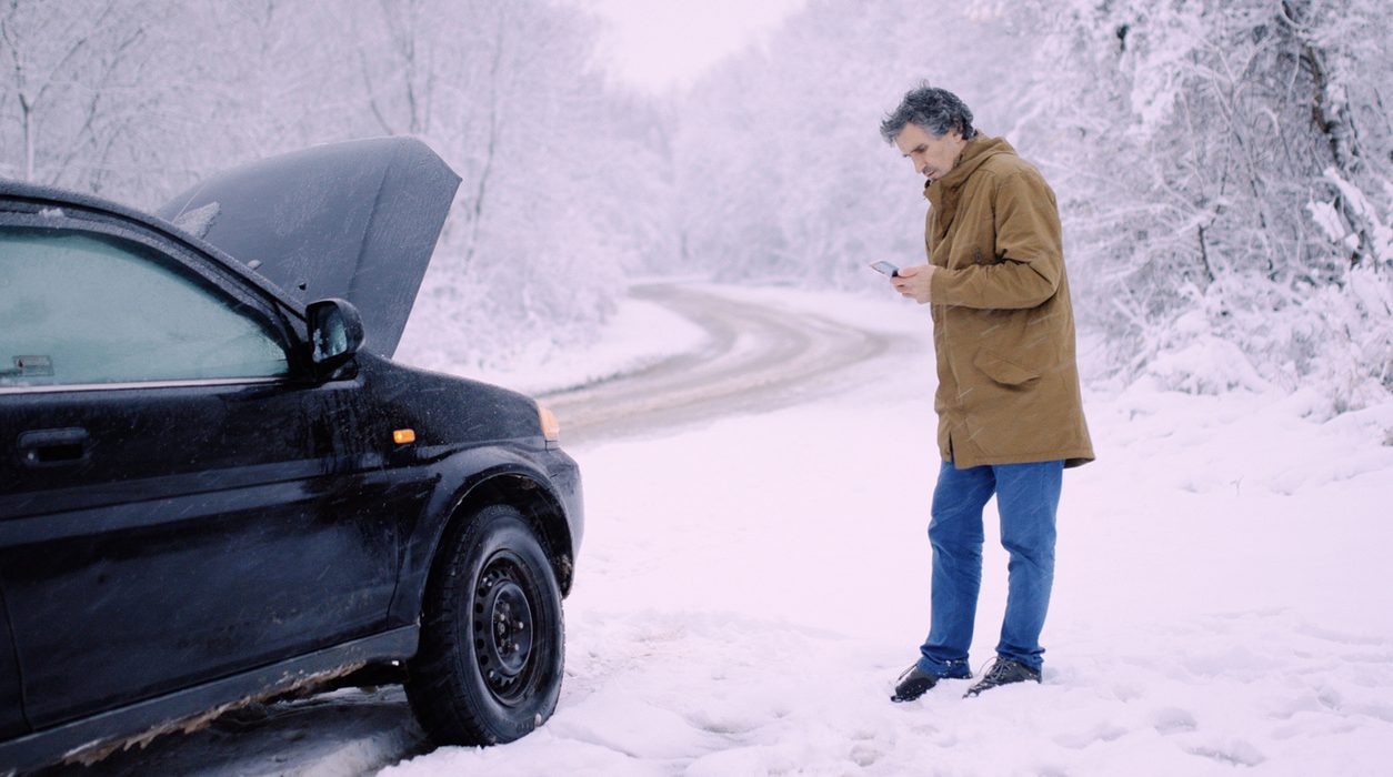 Driver on the phone beside a car on a snowy roadside