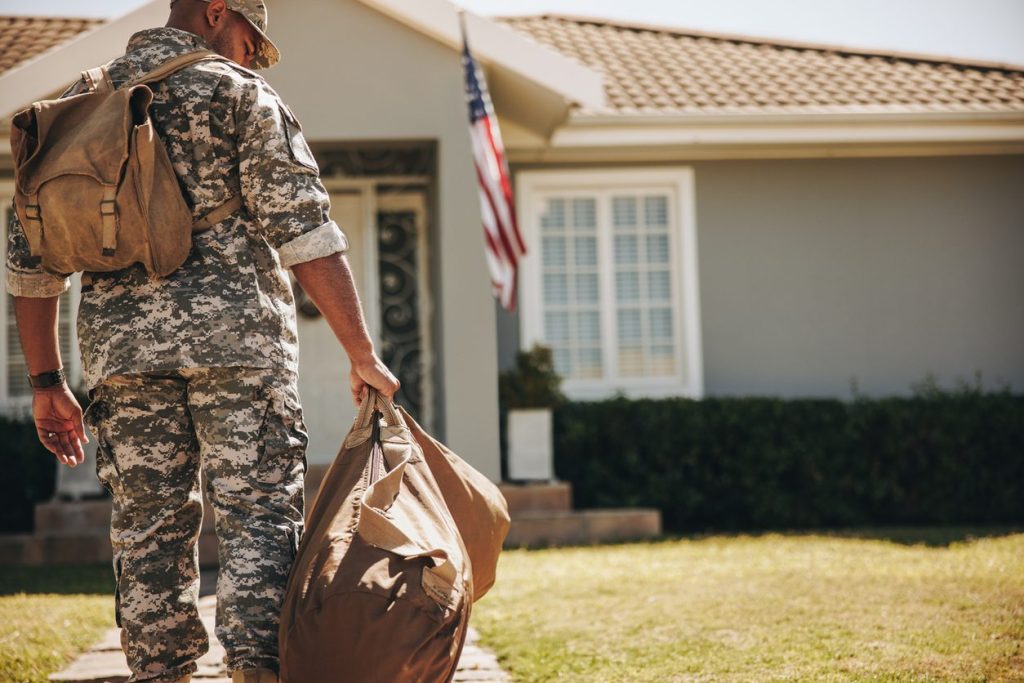 Service member arriving home at a house flying the American flag