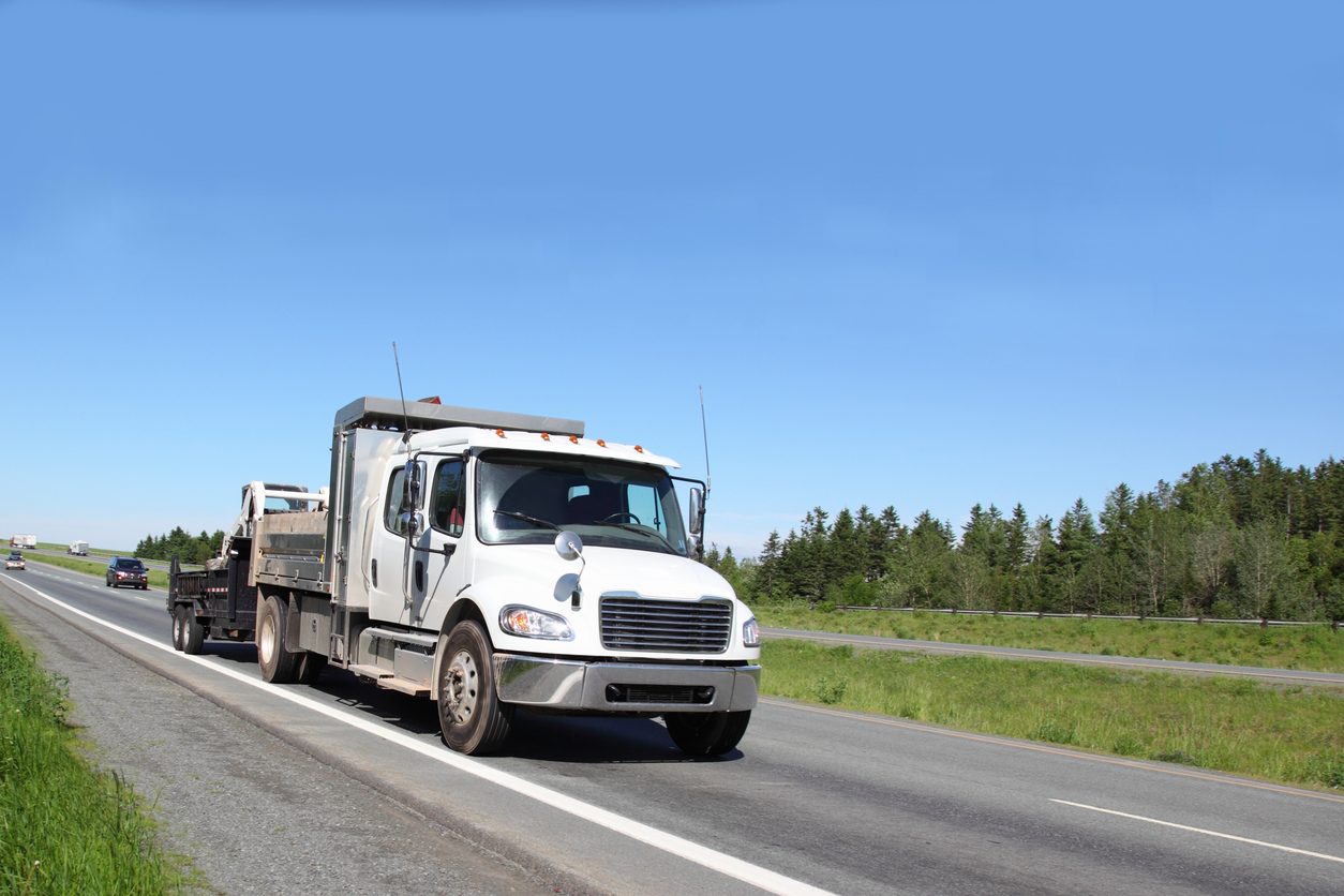 White truck towing a loaded trailer on a highway