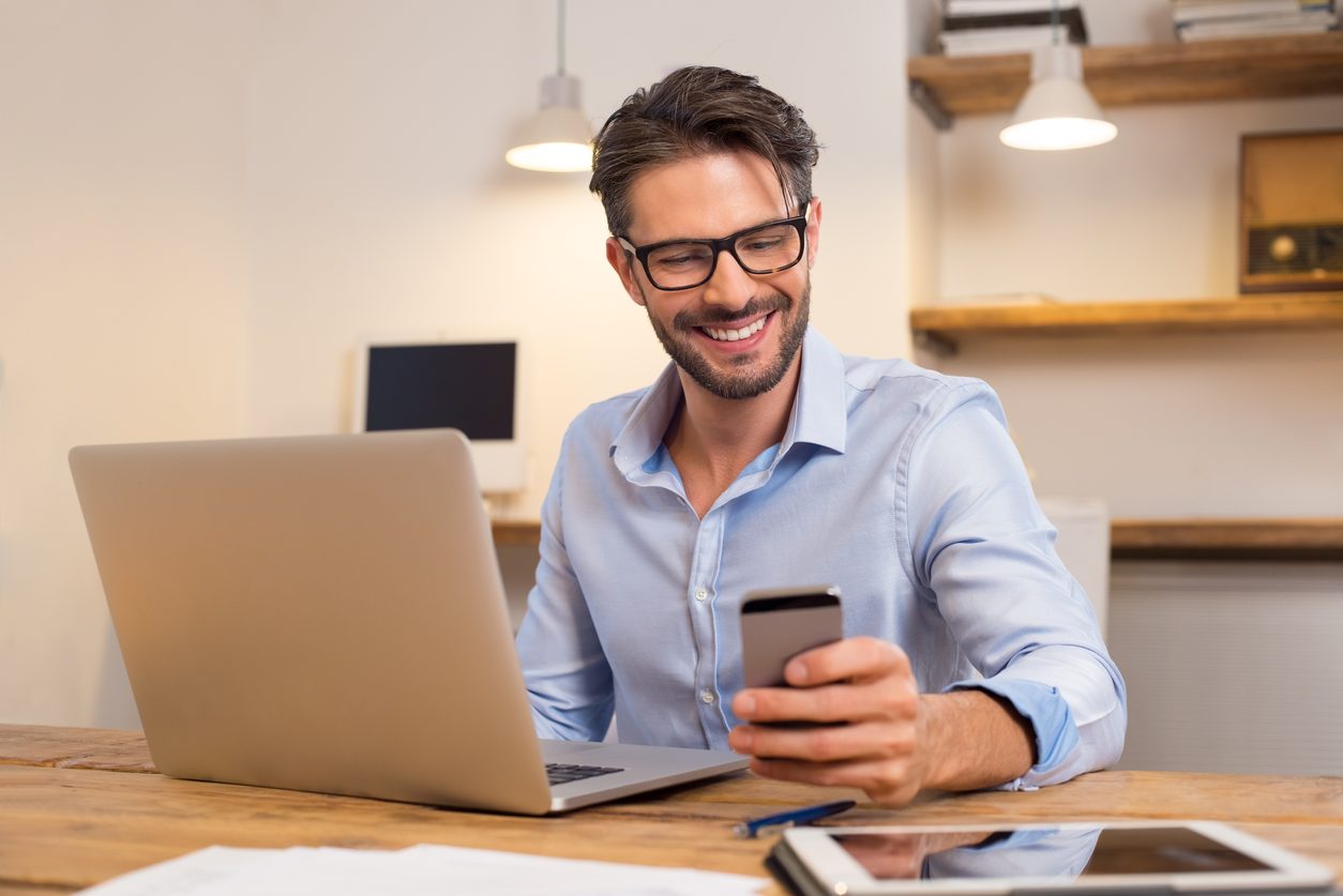 Person checking a phone beside a laptop at a desk