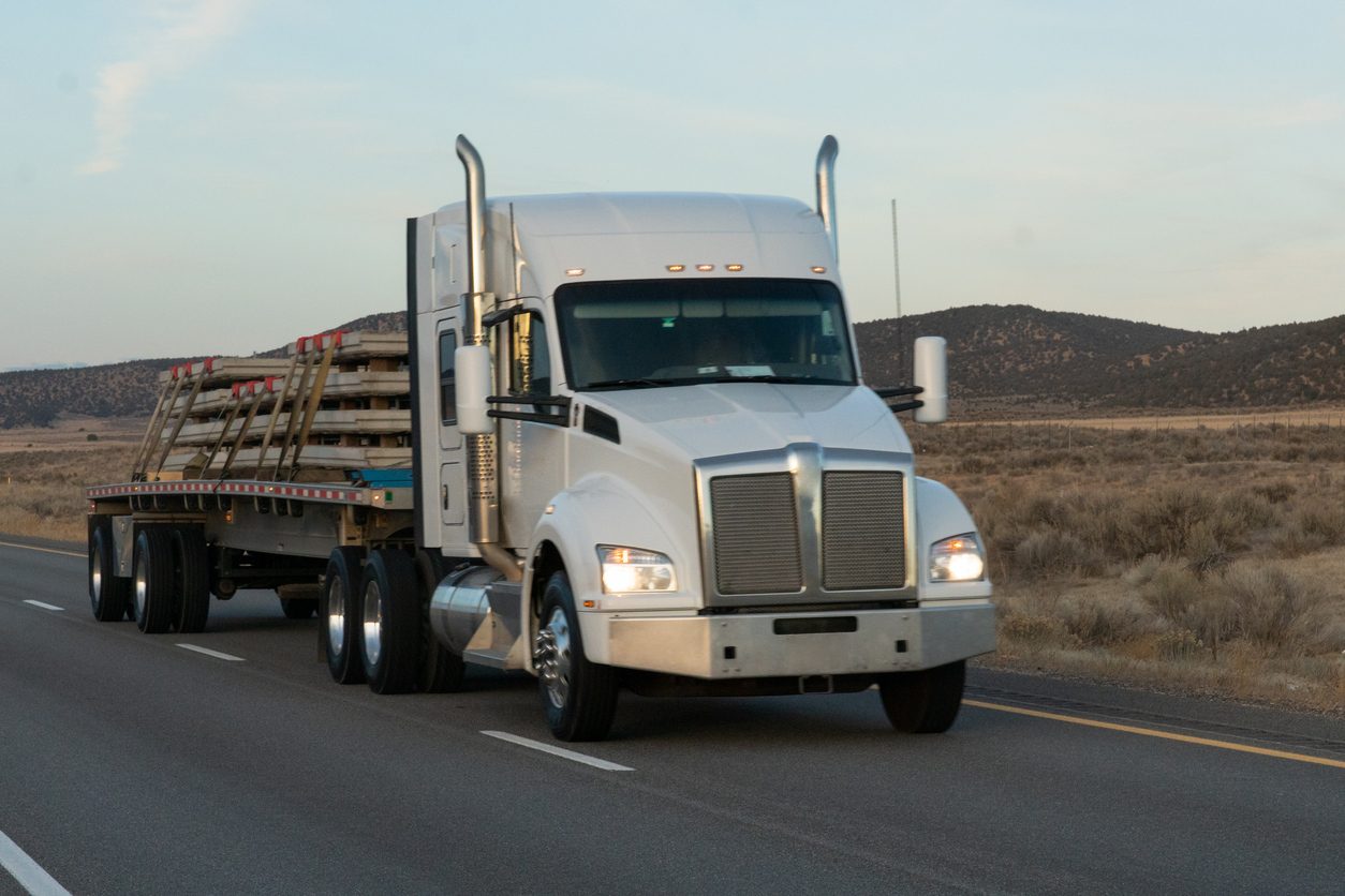 White conventional tractor with a flatbed trailer on a rural highway