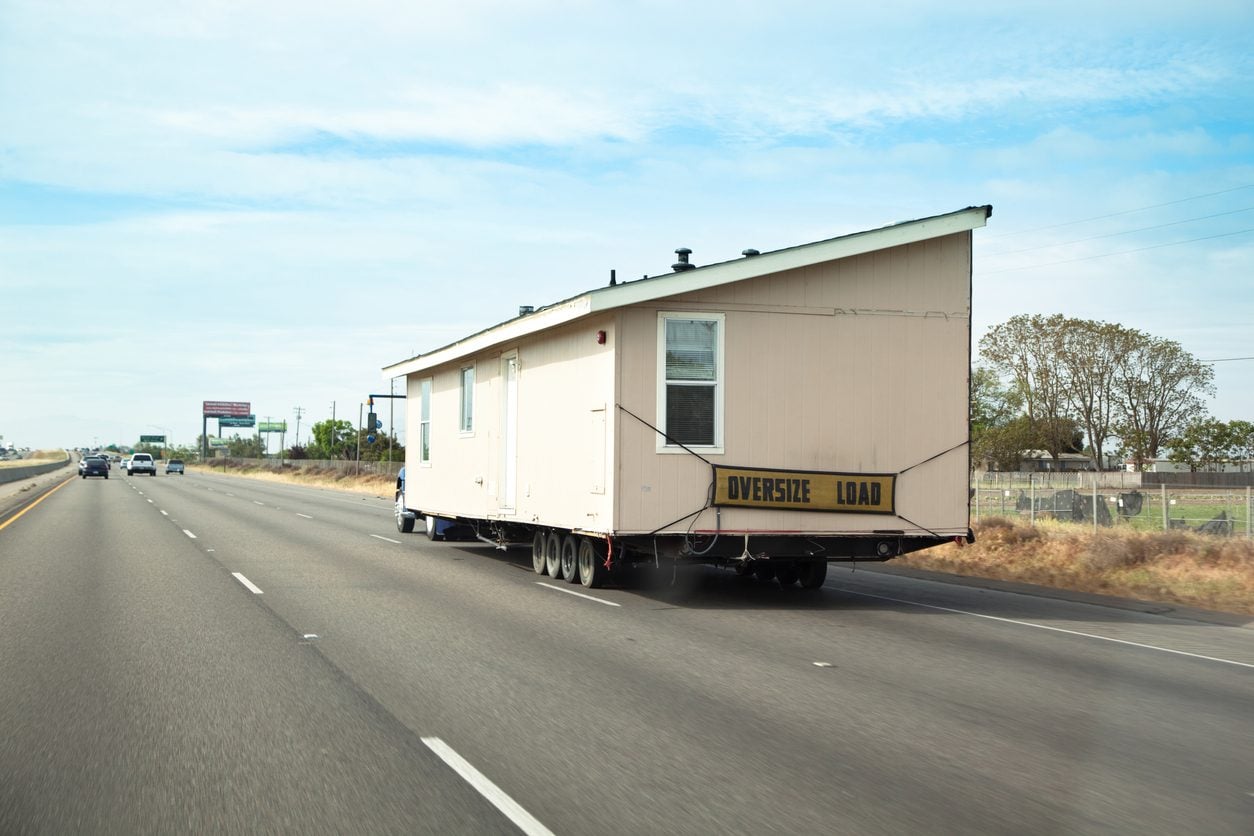 Mobile home section on a trailer with an oversize load banner