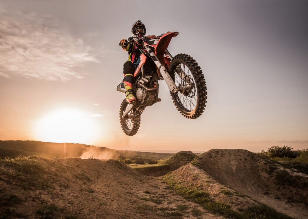 Motocross rider mid jump over a dirt berm at sunset