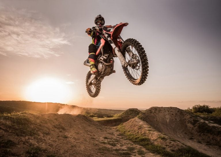 Motocross rider mid jump over a dirt berm at sunset