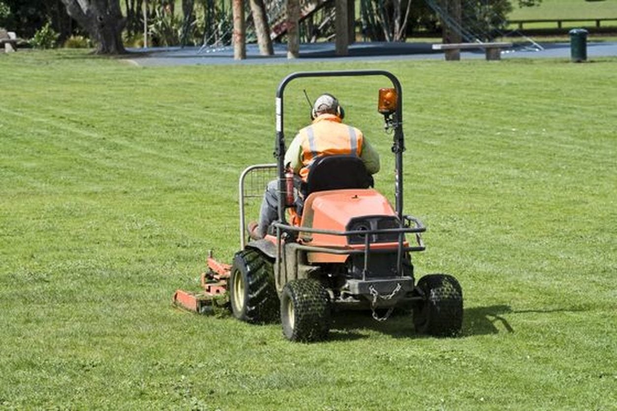 Operator cutting grass on an orange commercial ride on mower
