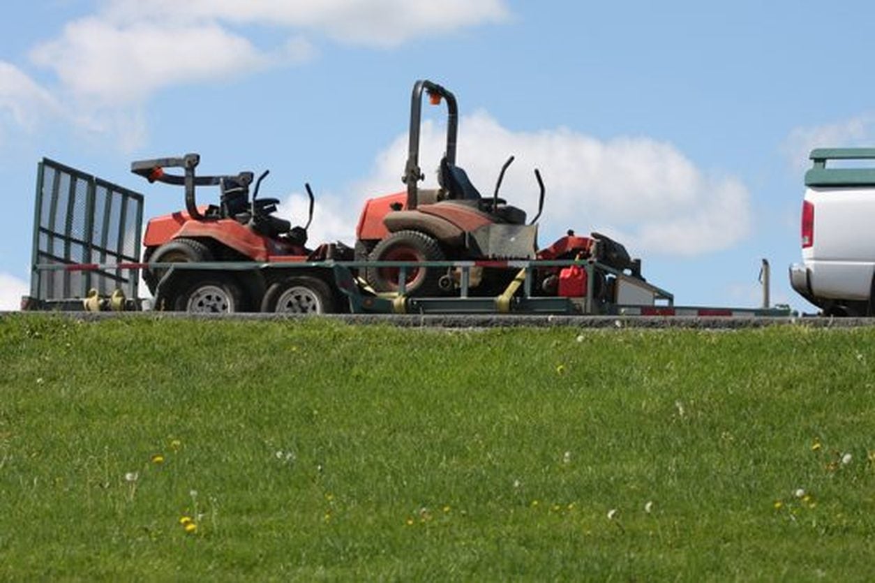 Two ride on mowers strapped to a trailer behind a pickup truck