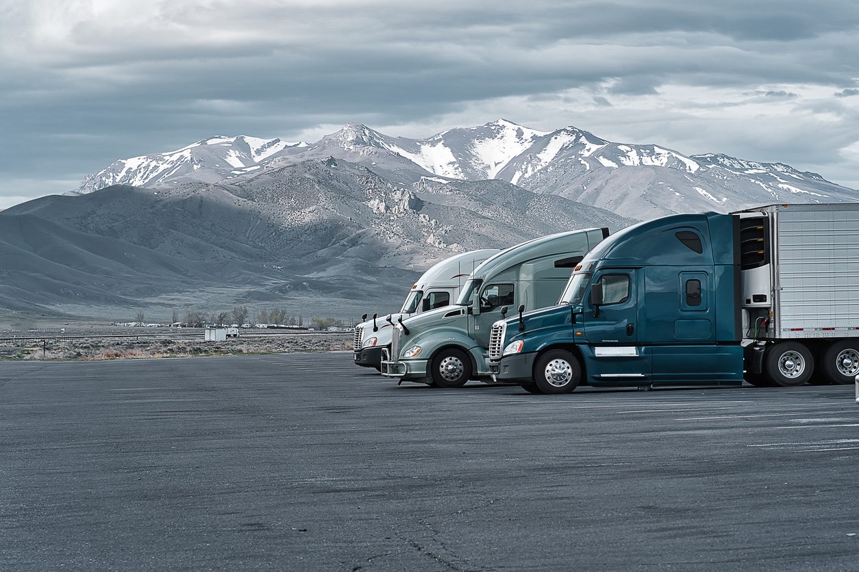 Conventional tractors parked at a truck stop below snow capped mountains