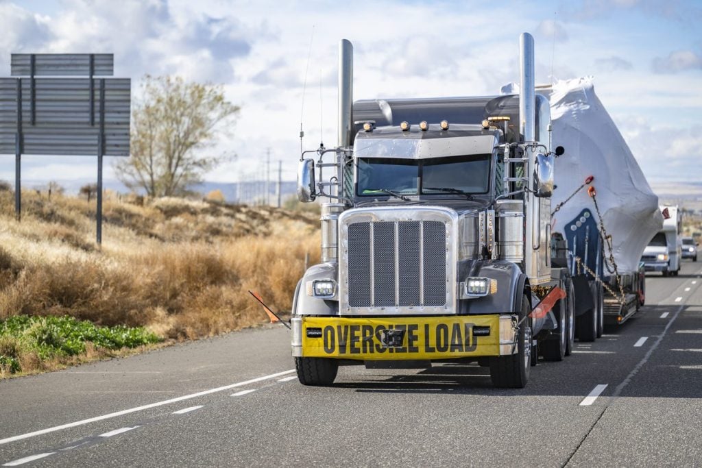 Semi truck with an oversize load banner hauling covered cargo on a step deck trailer
