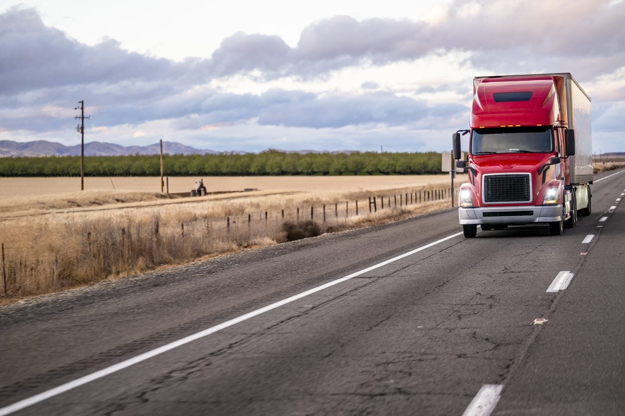 Red conventional tractor with a dry van on a straight highway