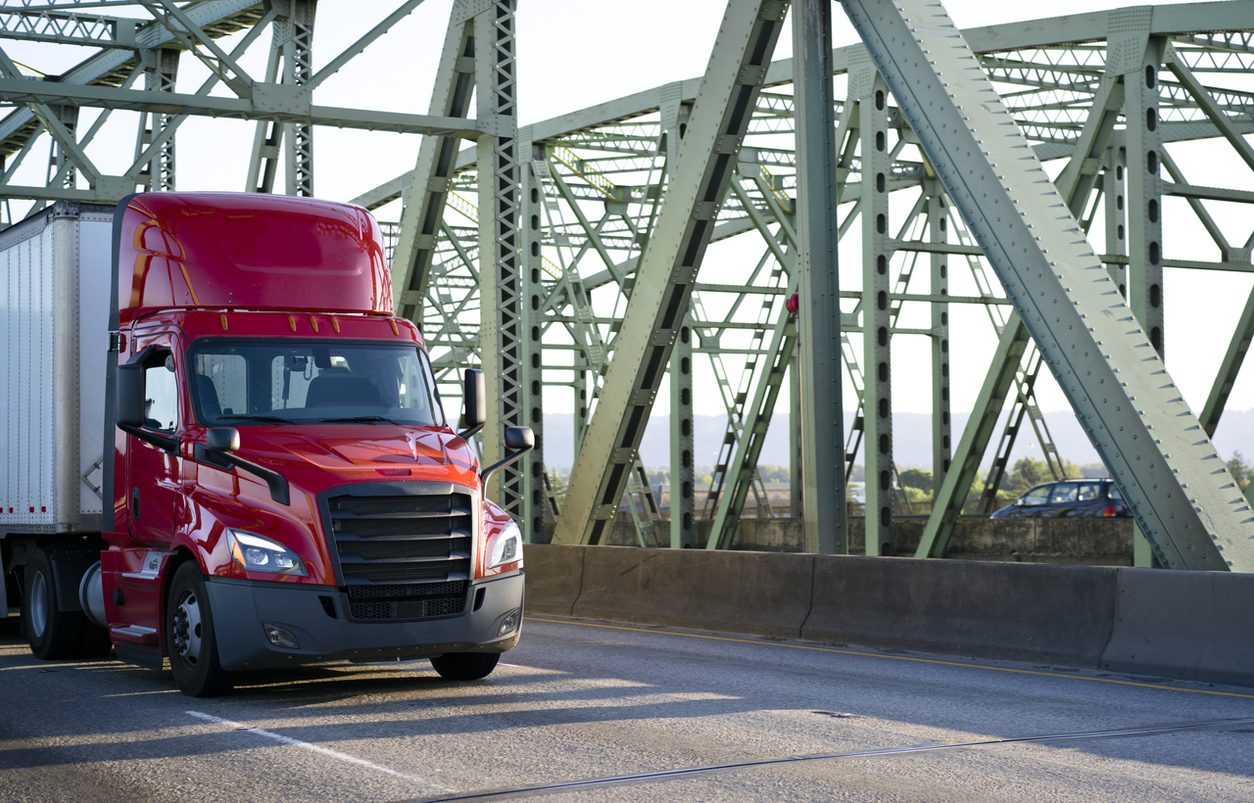 Red day cab tractor crossing a steel truss bridge